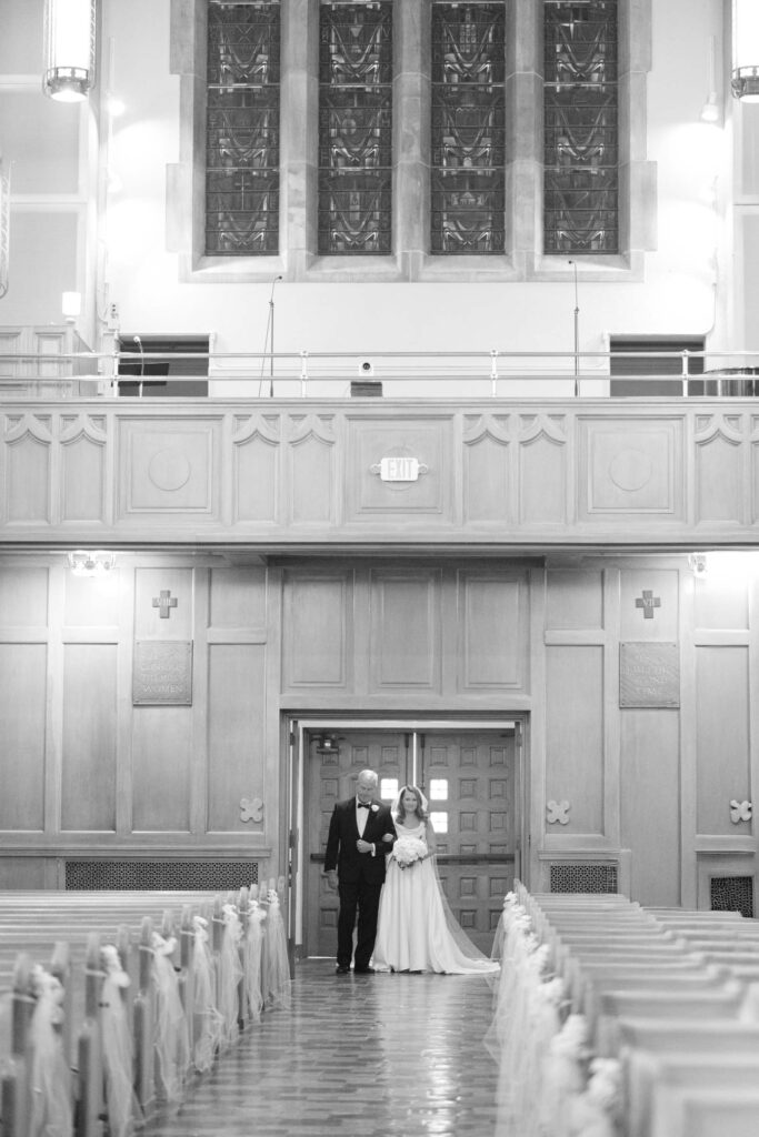 Black and white photo of bride walking down the aisle with her father inside a Kansas City church