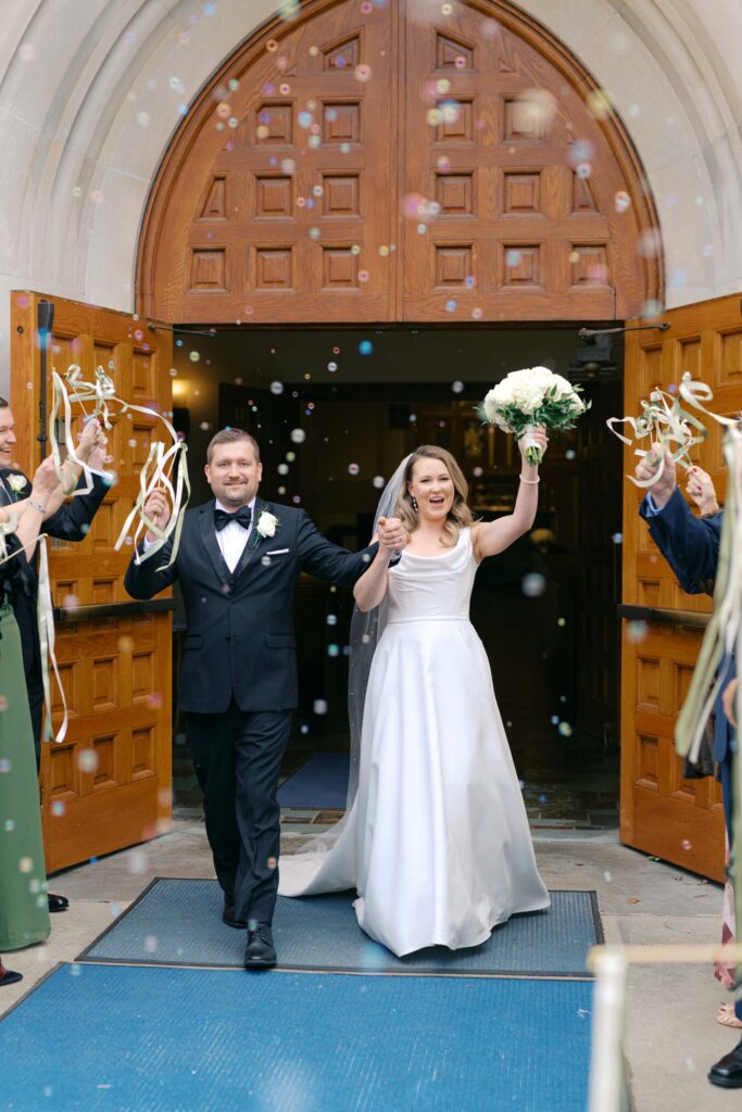 Bride and groom celebrating as they exit the church surrounded by guests blowing bubbles