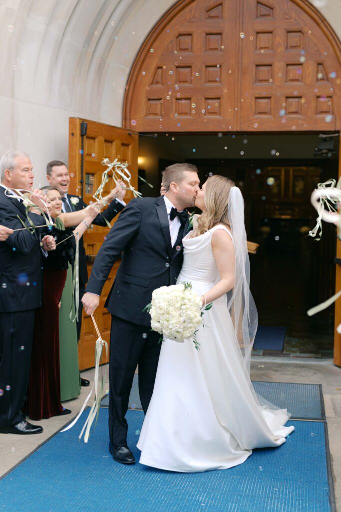 Bride and groom kissing during their joyful bubble exit outside the church after the ceremony