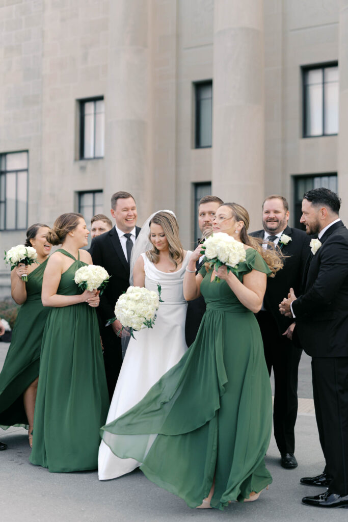 Bridesmaids laughing together while holding white rose bouquets during wedding portraits
