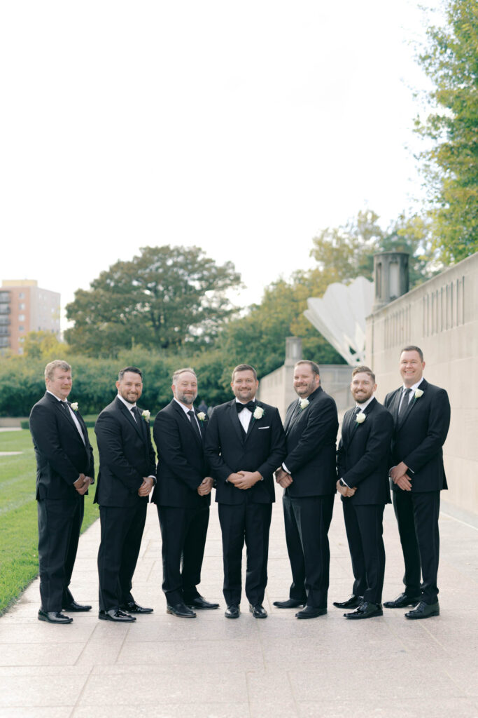 Groom posing with his groomsmen in black tuxedos during wedding portraits