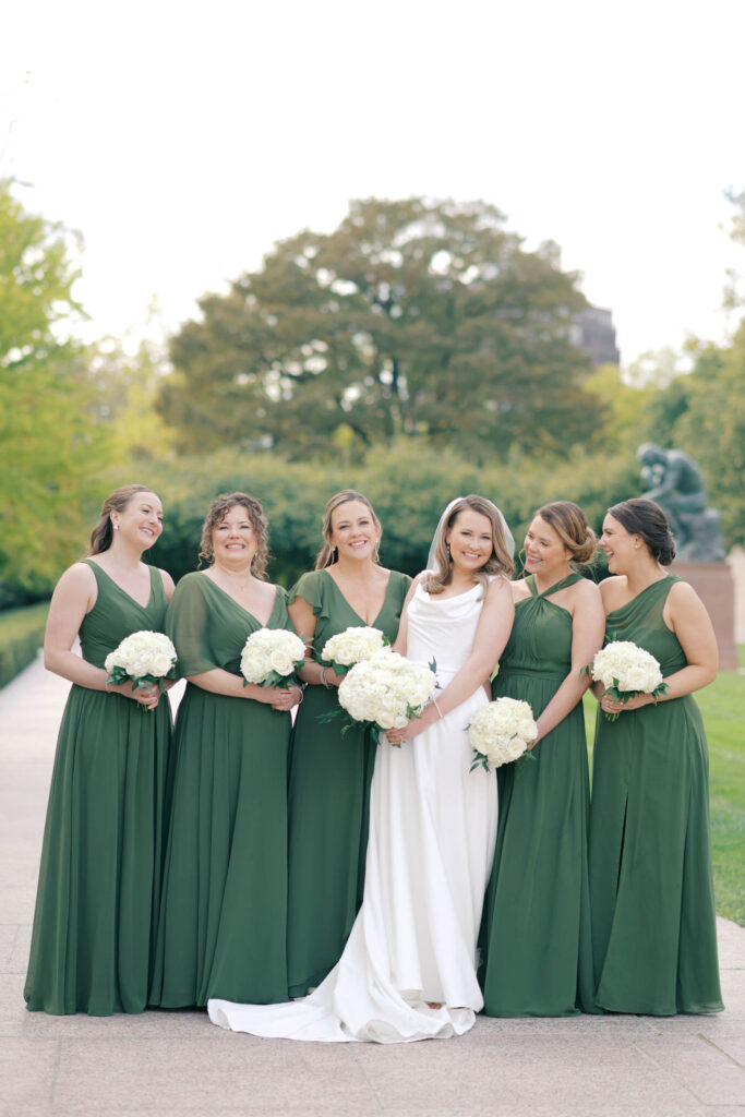 Bride smiling with her bridesmaids in green dresses holding white rose bouquets