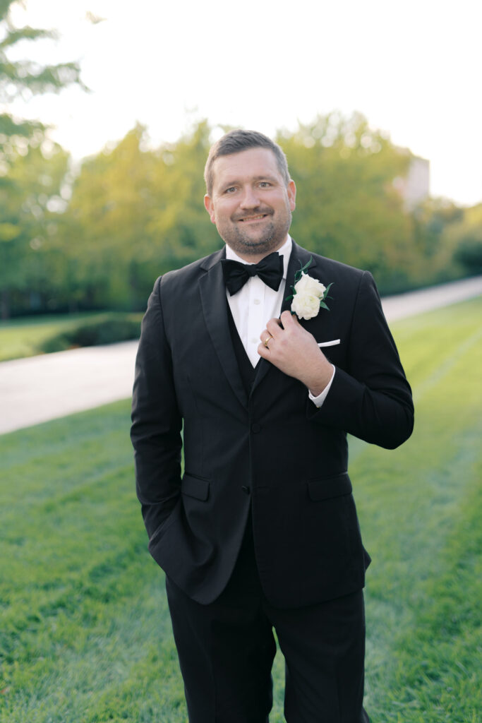 Portrait of the groom in a black tuxedo with a white rose boutonniere outdoors