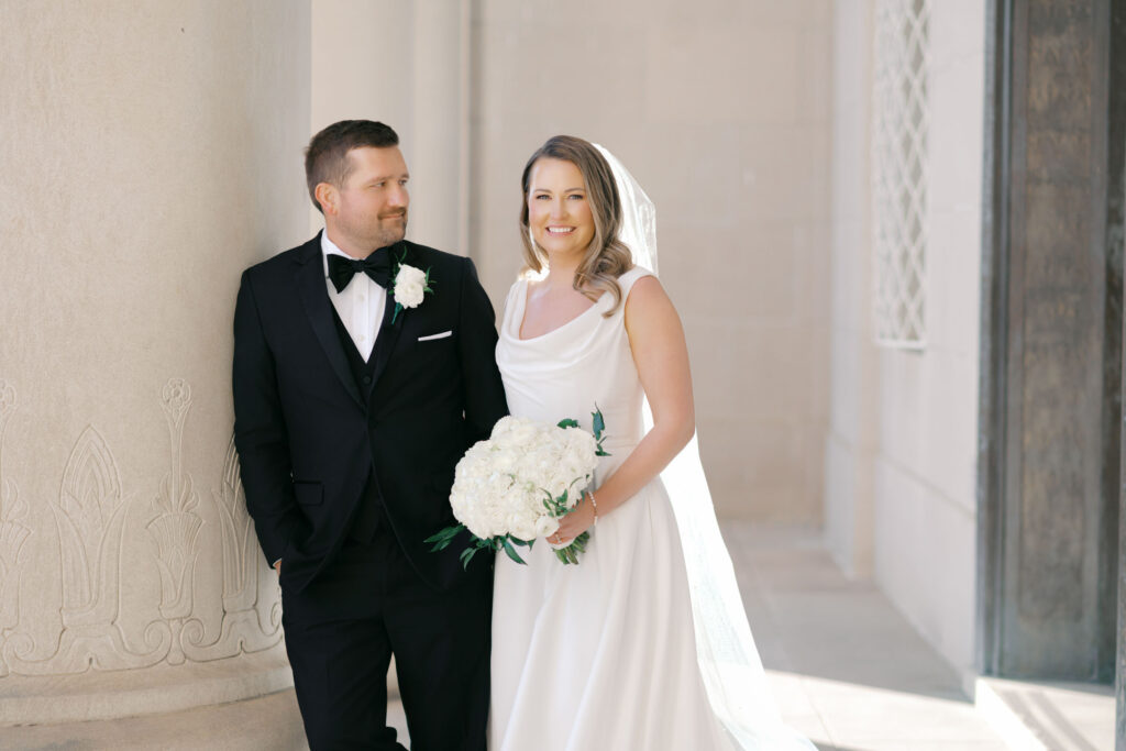 Bride and groom standing together beneath stone columns during Kansas City wedding portraits