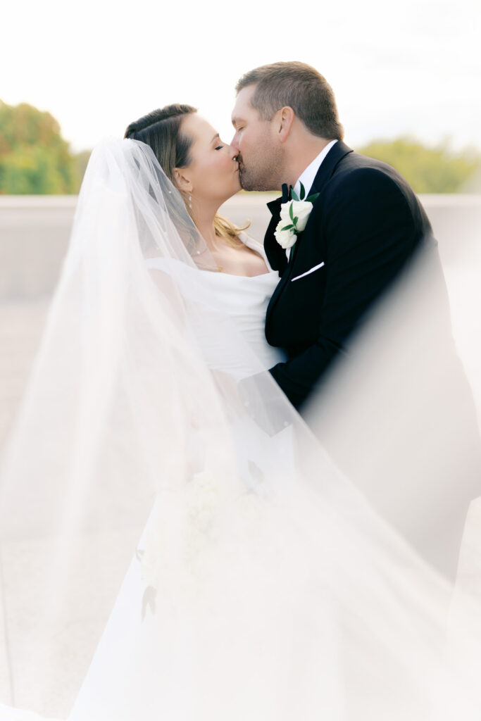 Romantic wedding portrait of bride and groom kissing with the bride’s veil flowing in the wind