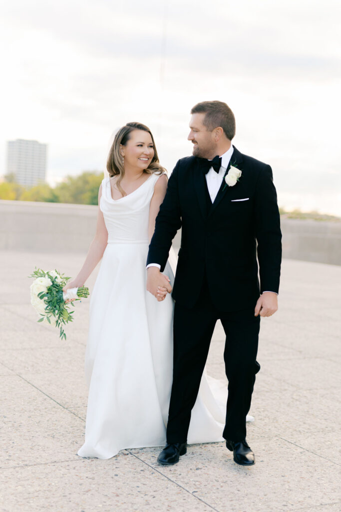 Bride and groom walking together with the Kansas City skyline softly visible in the background