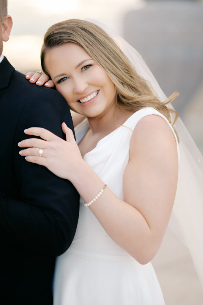 Close-up portrait of the bride smiling while resting her head on the groom’s shoulder