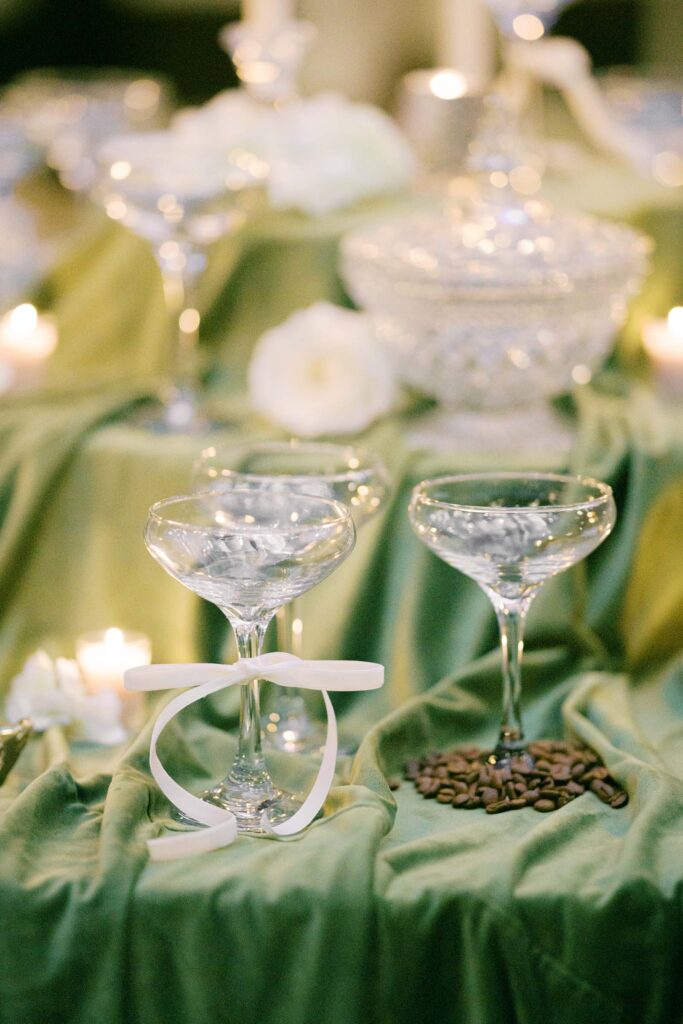 Elegant wedding cocktail table with champagne coupe glasses and green linen