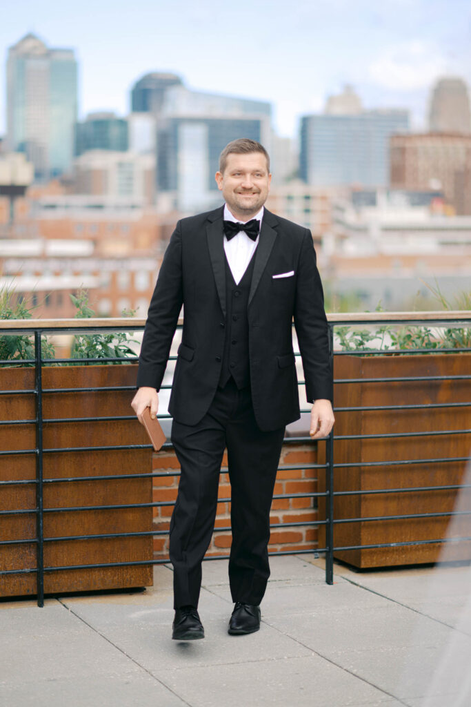 Groom walking on the Crossroads Hotel rooftop with the Kansas City skyline in the background