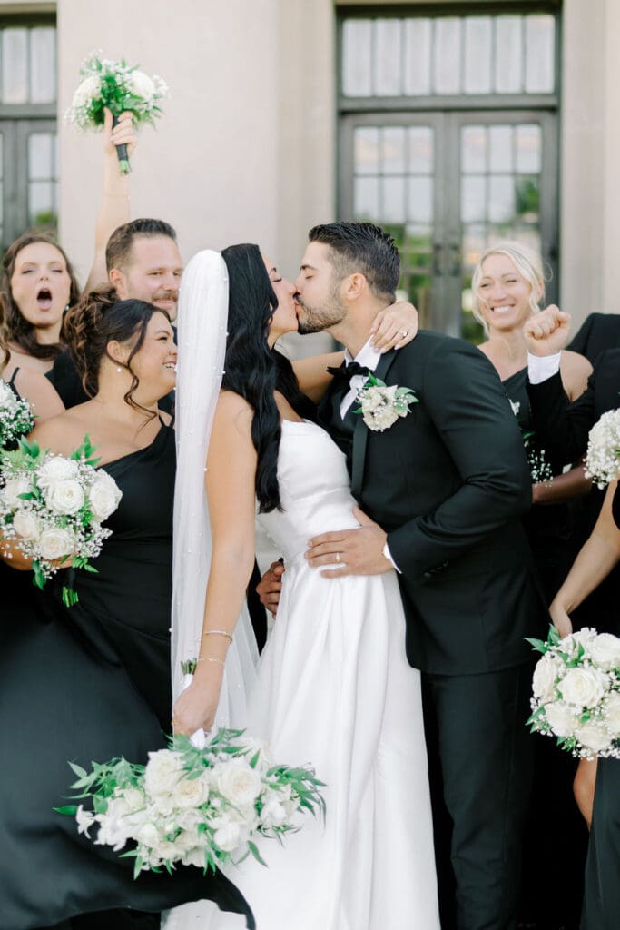 bride and groom kissing with bridal party surrounded at the nelson atkins in kansas city